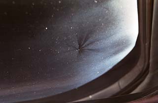 Ding in flight deck window caused by high velocity impact from debris.